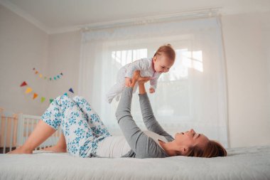 Mutlu anne bebeği kucağına aldı, yatağa uzandı. Yan görüş. Annelik ve çocuk bakımı kavramı.
