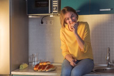 Diyetten vazgeçme konsepti. Genç bir kadın açgözlülükle pasta yiyor. Mutfaktaki masada oturuyor..