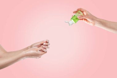Dezenfeksiyon ve bakteri ve virüslerden korunma kavramı. Kadınların elleri altta sabunla, kadınların elleri üstte antibakteriyel jelle yıkanır. Eller yakın plan. Pembe arka plan..