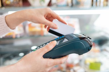 Kadın ödemeyi tamamlamak için ödeme makinesinden bir banka kartı geçirir. Eller yakın çekim ve yan görüş. NFC konsepti, iş ve bankacılık operasyonları.