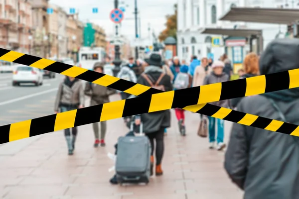 Do not cross.Barrier tape-quarantine,isolation.A girl with a suitcase behind him walking on the sidewalk through a crowd of people.Rear view. The concept of coronavirus and quarantine.