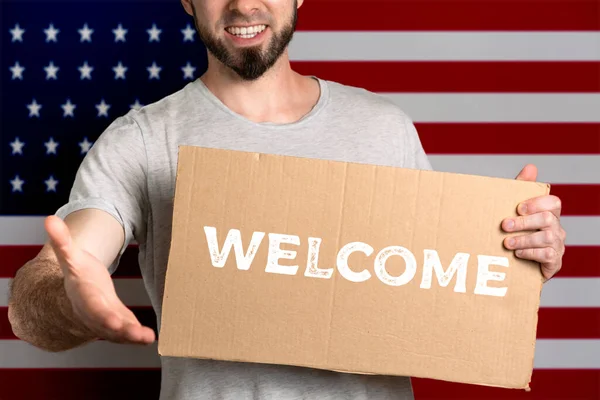 移民と異なる人生の位置の人々のための寛容の概念 男は段ボールを持っていて 挨拶のために手を伸ばしている アメリカの国旗 テキストようこそ — ストック写真