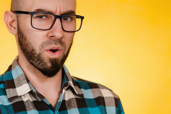 人和情感 一个留着胡子 戴着眼镜 穿着蓝色格子衬衫的男人用不满意的声音问了些什么 黄色背景 复制空间 — 图库照片