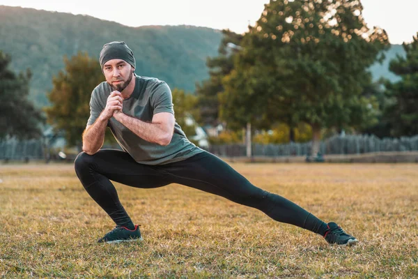 Sports and yoga. A man in sportswear performs stretching on the grass before training.