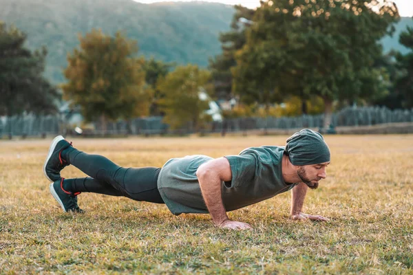 Sports and yoga. A man in sportswear push-ups during training. Park and trees on the background. View at profile.