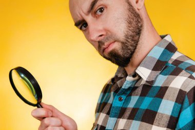 Sorun bulma ve çözme kavramı. Mavi ekose gömlek giymiş, elinde büyüteçle dikkatlice bakan kel bir adam. Boşluğu kopyala.
