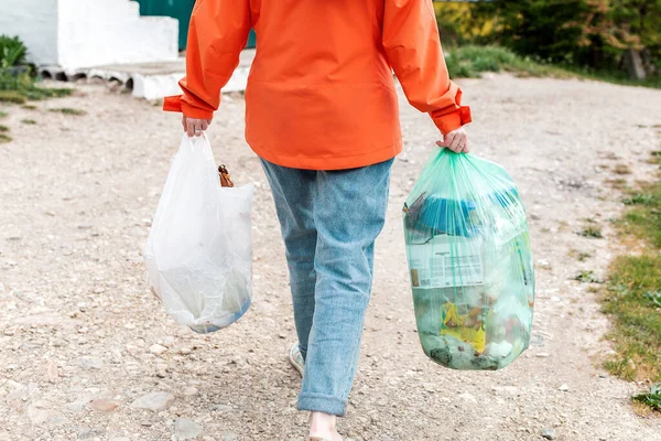 Garbage. The woman goes with two bags of garbage to throw them into the container. Outdoor. Rear view and close up. Concept of pollution environmental pollution and zero waste.