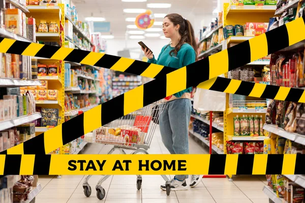 Do not cross.Barrier tape-quarantine,isolation.A young smiling Caucasian woman rolls a grocery cart around the store and uses a mobile phone. The concept of coronavirus and quarantine.