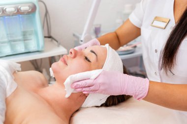 Lastik eldivenli kozmetolog müşteriye özel peçeteler kullanarak yüz masajı yapıyor. Yan görüş. Kozmetoloji ve tedavi kavramı.