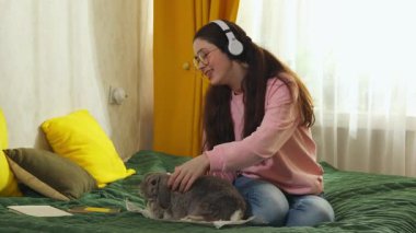 Genç beyaz kadın tavşan kürkünü dikkatlice kırpıyor yatağın üzerinde küçük bir makasla, tımar, hijyen ve evcil hayvan bakımı konseptiyle..