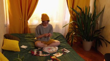 Genç, beyaz bir kadın evinde yatağında oturmuş halkayla çember nakış işliyor yaratıcı hobisinin keyfini çıkarıyor ve rahat yatak odasında dinleniyor. Geniş açı.