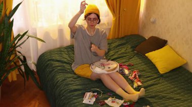 Çekici beyaz kadın evde yatakta nakış nakışlı halka örgülerle oturur ve iç mekanda yaratıcı hobilerini sakinleştirmekten zevk alır. Üst görünüm.