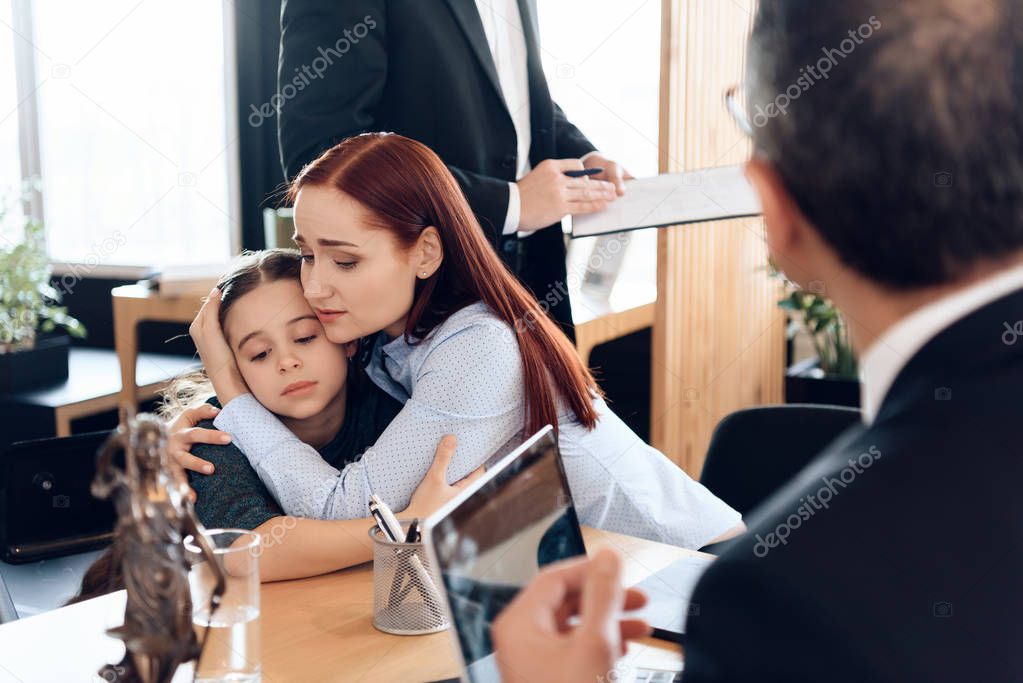 Young sad mother hugging little upset daughter sitting in lawyer office for divorce