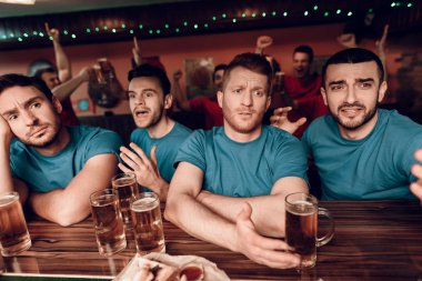 Diğer fanlar kutluyor ve arka plan üzerinde tezahürat yaparken spor barda oturan üzgün mavi takım taraftarları