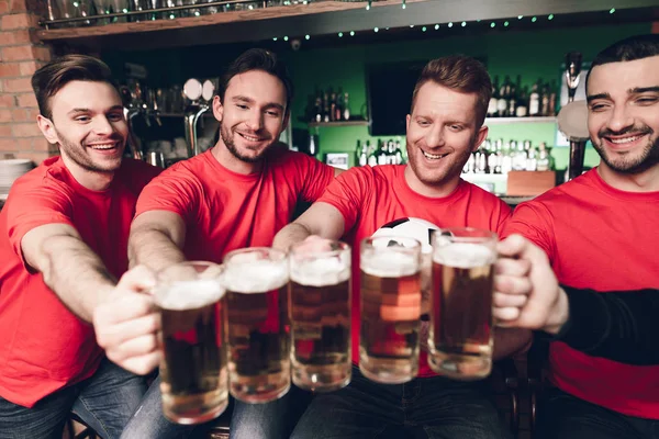 Soccer fans watching game and drinking beer at sports bar, red team supporting