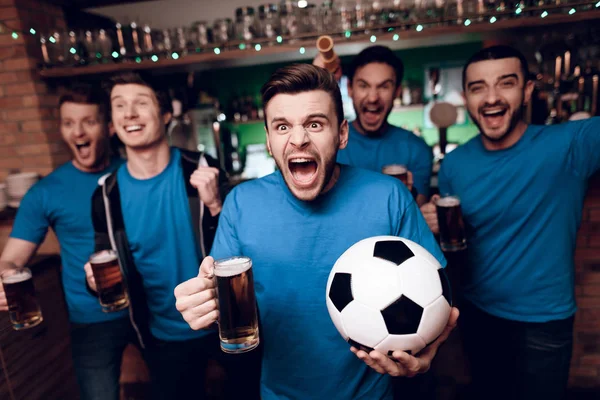 Group of soccer fans watching game and drinking beer at sports bar at evening