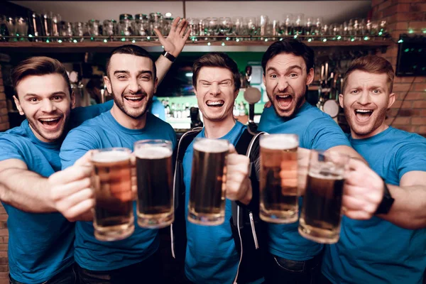 Group of soccer fans watching game and drinking beer at sports bar at evening