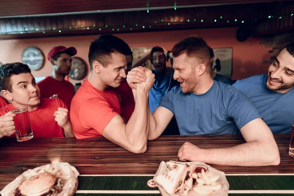 Bilek güreşi spor barında yarışan mavi ve kırmızı takım taraftarları 