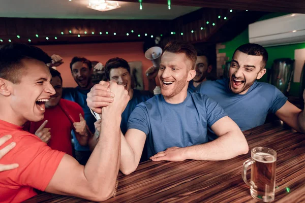 Blue and red team fans competing in arm wrestling at sports bar