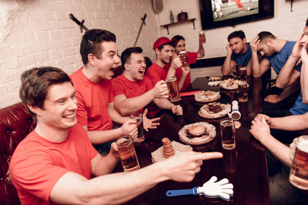 Болельщики красной команды аплодируют, в то время как противники сидят грустно в спортивном баре
