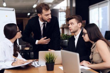 Şirket başkanı toplantı sırasında diğer çalışanlarla görüşür. İş kıyafetleri giymişler. İş hakkında konuşuyorlar..