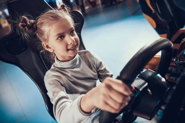 Menina sentada ao volante de uma máquina de jogo. — Fotografia de Stock