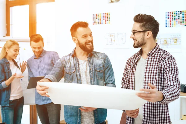 Zwei Designer halten ein großes Blatt Papier in der Hand. — Stockfoto