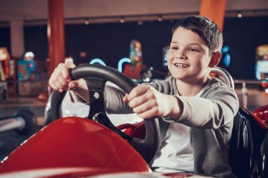 Little boy sitting behind the wheel of a toy car. clipart