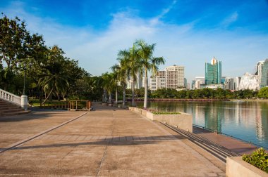 bangkok merkezinde gün batımı ışıkları büyük göl boyunca güzel kaldırım, Bangkok parklarından birinde yürüyüş yolu, palmiye ve göl ve arka planda gökdelenler ile park manzara