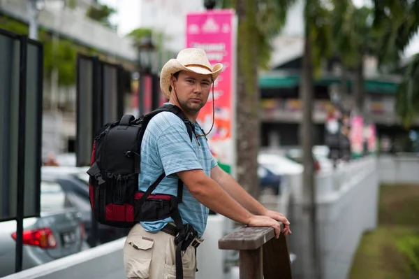 adult man with big backpack is looking straight to camera, tourist traveling in asia, big guy with bag is waiting for bus