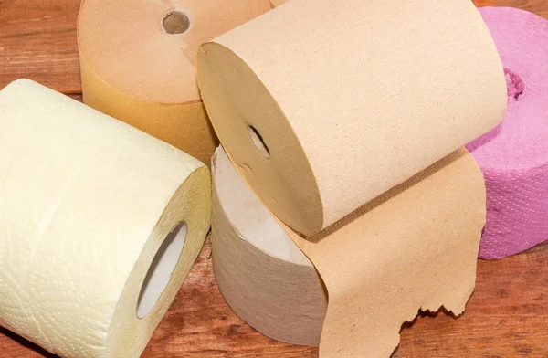 Fragment of pile of several rolls of various toilet paper different quality and colors closeup on a dark wooden surface