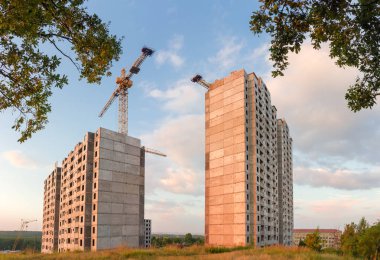 Kule vinç ve ağaçlar karşı ön planda gökyüzünün gün batımında bina ile prekast beton panelleri çok hikaye Konut Evleri inşaatı Panoraması