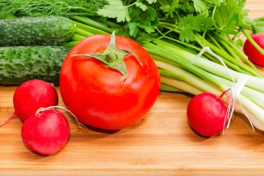 Yıkanmış ve soyulmuş yeşil soğan, domates, salatalık, kırmızı turp, dereotu, maydanoz bambu kesme tahtası portre üzerinde parçası