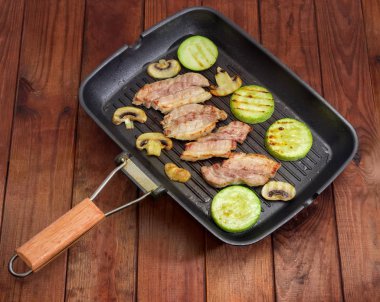 Eski bir ahşap rustik masa üzerinde ızgara dilim çizgili domuz pastırması, sebze iliği ve mantar ızgara tava