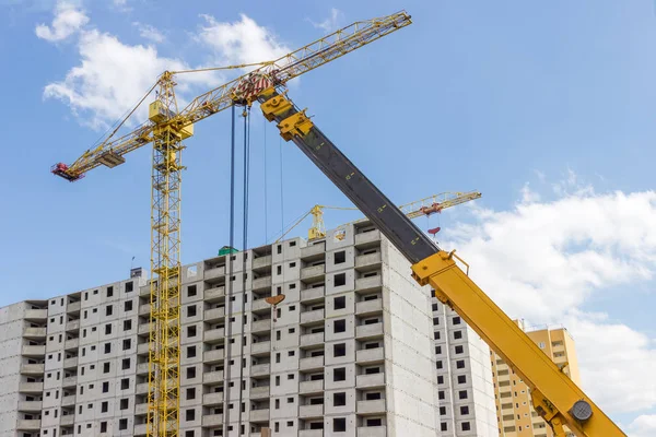 Boom lift with telescoping boom and tower cranes with lattice booms on a construction of multi story house from precast concrete panels