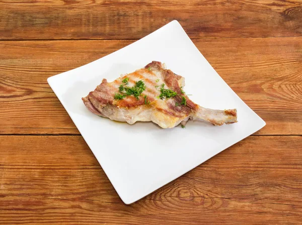 Izgara Domuz loin pirzola ile kısmen kaburga frenched ve beyaz kare tabak üzerinde ahşap rustik masa üzerine kıyılmış dereotu serpilir