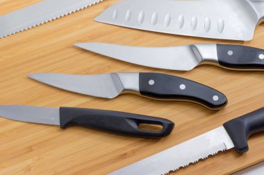 Fragment of wooden bamboo cutting board with several different kitchen knives on it closeup clipart