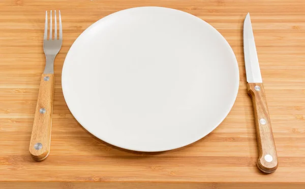 竹木表面空圆白碟的背景与木柄不锈钢制刀叉组成的餐具 — 图库照片