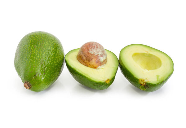 One green-skinned pear-shaped avocado cut in half and one whole avocado on a white background