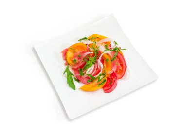 Taze dilimlenmiş kırmızı ve sarı domates, soğan ve yeşillik üzerinde beyaz bir arka plan üzerinde beyaz kare tabak sebze salatası