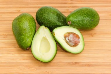 Bir yeşil derili armut biçimli avokado kesilmiş bambu kesme tahtası üzerinde yarım ve birkaç bütün avokado