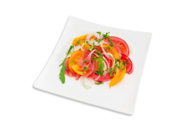 Taze dilimlenmiş kırmızı ve sarı domates, soğan ve yeşillik üzerinde beyaz bir arka plan üzerinde beyaz kare tabak sebze salatası