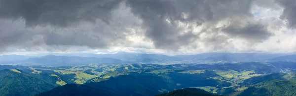 Top view of the mountain ranges and valleys with villages in the Carpathian Mountains on background of the sky with clouds. Summer wide panorama, Ukraine