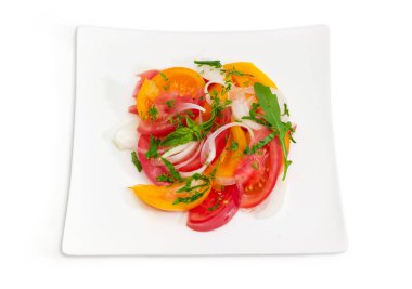 Sebze salatası, taze dilimlenmiş kırmızı ve sarı domates, soğan ve Yeşiller üstten görünüm üzerinde beyaz bir arka plan üzerinde beyaz kare tabak