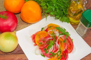 Taze dilimlenmiş kırmızı ve sarı domates, soğan ve onun hazırlanması için malzemelerin arasında yeşil sebze salatası ile beyaz kare tabak parçasının üstten görünüm