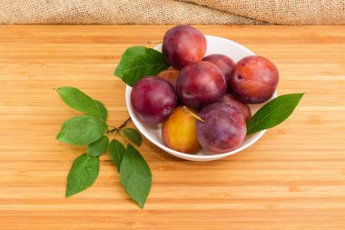 Beyaz kase ve bir bambu ahşap yüzeyde erik ağacının yaprakları olgun mor Erik