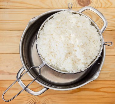 Paslanmaz çelik elek ile üstten görünüm haşlanmış ve paslanmaz çelik stok pot bir açık renkli ahşap yüzeyde beyaz pirinç yıkanır