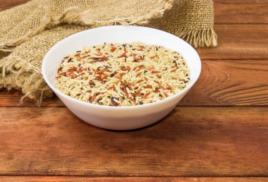 Çiğ uzun taneli kahverengi, kırmızı ve siyah pirinç bir masada koyu renkli ahşap rustik çuval bezi beyaz bir kase karışımı