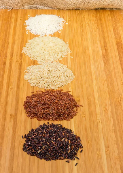 Bamboo cutting board with piles of the raw short-grained white and parboiled rice, long-grained brown, red and black rice