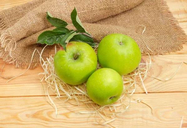 Ripe green apples and small apple tree twig with leaves on a light colored wooden rustic table